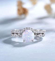 a white opal and diamond ring sitting on top of a table