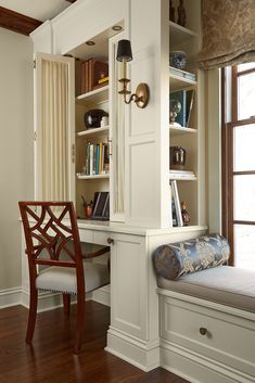 a room with a window seat, desk and bookcases on the wall next to it