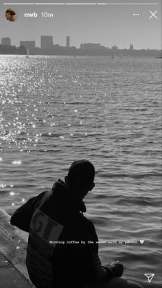 a man sitting on the edge of a pier next to water