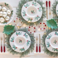 a table set for christmas with plates, silverware and holly wreaths on it