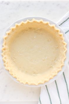 an uncooked pie crust in a white bowl on a green and white towel