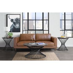 a brown leather couch sitting in front of a window next to two tables with candles on them