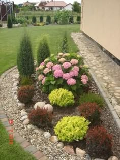 a garden with rocks and flowers in the center, along side a home's driveway