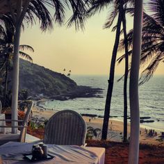 an outdoor dining area overlooking the ocean with palm trees and people on the beach in the distance