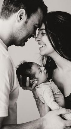 a man and woman holding a baby in their arms while looking at each other's eyes