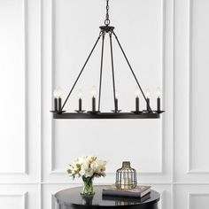 a chandelier hanging over a table with flowers and books on the table next to it