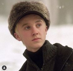 a young man wearing a fur hat and black jacket looking at something in the distance