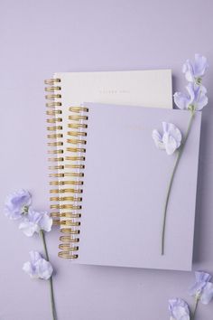 two spiral notebooks sitting next to each other on top of a table with flowers