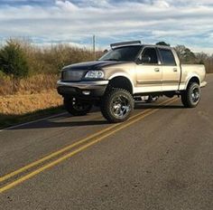 the truck is parked on the side of the road in front of some grass and bushes