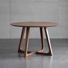 a round wooden table sitting on top of a cement floor next to a white wall