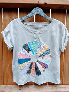 a t - shirt hanging on a wooden fence with an assortment of different colored fabrics