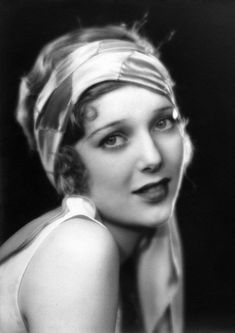 an old black and white photo of a woman with a scarf on her head, looking at the camera