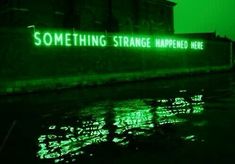 a neon sign that reads something strange happened here on the side of a building next to water