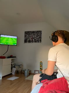 a person sitting on a couch with headphones in their ears watching a soccer game