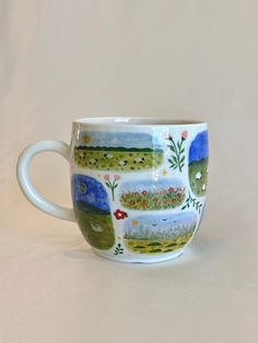 a coffee cup with an image of the countryside on it's side, sitting on a white surface