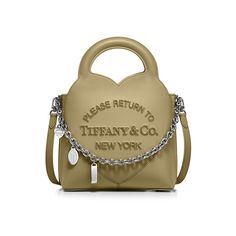 Inspired by one of the House’s most distinctive designs, the heart-shaped Return to Tiffany® handbags are crafted in supple leather and embellished with charm and chain link accents that nod to our iconic jewelry. Add a playful touch to every day with this mini charm tote. It features a detachable leather strap and an interior zip pocket that keeps essentials organized. Khaki calfskin leather; 7.9" W x 11" H x 3.9" D; Palladium-plated hardware, charms and chain link; Detachable leather strap and Iconic Jewelry, Return To Tiffany, Leather Tote Bags, International Jewelry, Mini Charm, Tote Bag Leather, Leather Shops, High Jewelry, Small Leather Goods