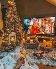 a person sitting in front of a christmas tree watching tv while holding a glass of wine