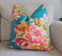 a colorful floral pillow sitting on top of a gray couch next to a white wall