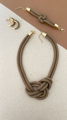 a brown rope necklace with two gold rings on it and a pair of earrings next to it