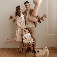 a man and woman are holding balloons while a baby sits in a chair with a dog