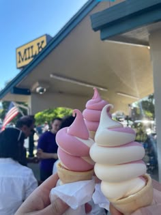 two ice cream cones with pink and white icing in front of a storefront