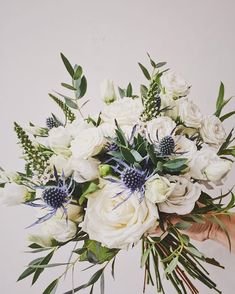 a bouquet of white flowers and greenery is held by someone's hand in front of a white wall