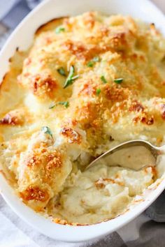 a close up of a casserole in a white dish with a serving spoon