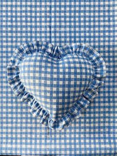 a blue and white checkered heart pillow on top of a tablecloth with ruffled edges