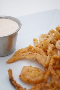 some fried food on a white plate next to a small bowl of ranch dips