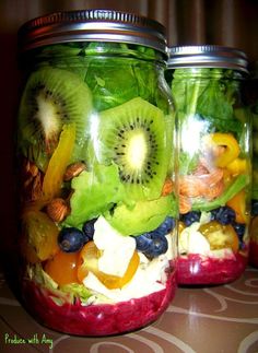 two mason jars filled with different types of fruit and veggies on top of a table