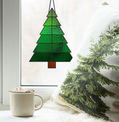 a green christmas tree hanging from a window sill next to a cup of coffee