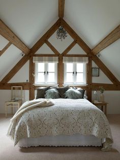 a large bed sitting under two windows next to a wooden table and chair on top of a carpeted floor