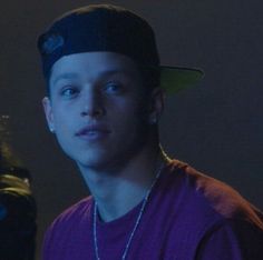 a young man in a purple shirt and black hat