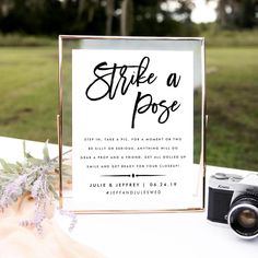 a sign that says strike a pose next to a camera and flowers on a table