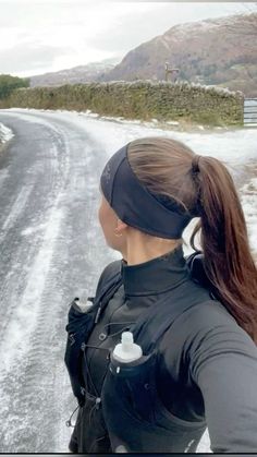 a woman standing on the side of a snow covered road with her back to the camera