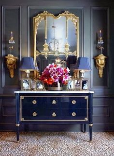 a table with flowers on it in front of a mirror and two gold sconces