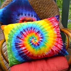 two colorful pillows sitting on top of a wicker chair