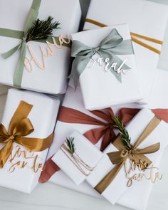 presents wrapped in white paper with gold and green ribbons tied around them, sitting on top of each other