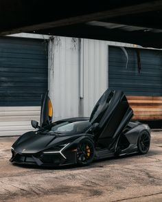 a black sports car with open doors parked in front of a garage door on the street