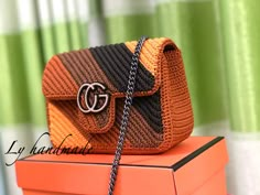 an orange and black purse sitting on top of a box next to a green curtain