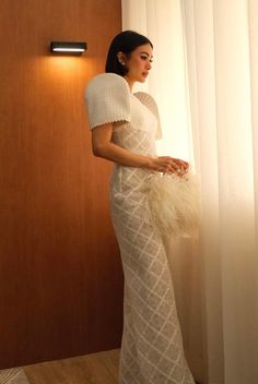 a woman standing in front of a window wearing a white dress with feathers on it