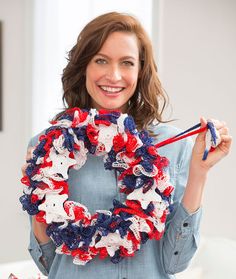 a woman holding up a patriotic wreath made from red, white and blue crocheted yarn