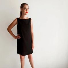 a woman standing in front of a white wall wearing a black dress and red lipstick