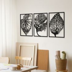 three framed art pieces hang on the wall above a dining room table with chairs and coffee cup