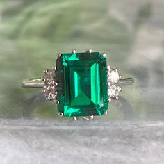 an emerald and diamond ring sitting on top of a table