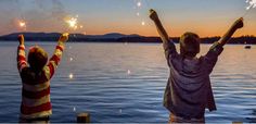 two people standing on a dock with their arms in the air while holding sparklers