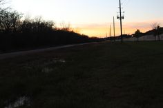 the sun is setting over an empty field with trees in the background and water puddles on the ground