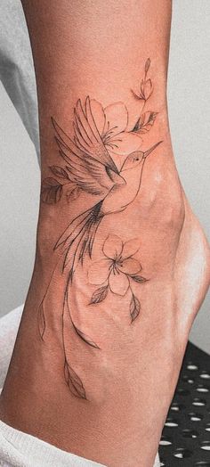 a woman's foot with a bird and flowers tattoo on the side of her ankle