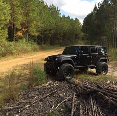 a black jeep is parked on the side of a dirt road in front of some trees