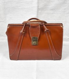 Original 1960s Vintage Rich Tan Leather Doctors Bag/Briefcase   This fantastic classic doctors bag is in a rich and warm brown leather. Brasstone metal push-lock closure and two carry handles. Very well made with reinforced stitching and extra leather panels. The original key is not attached but the case is unlocked and usable. Measures approx 16" x 11" x 7". Remnants of original travel/business stickers still present which adds to the character. There are some scratches and scuffs in keeping wi Brown Business Briefcase With Hasp Closure, Brown Briefcase With Hasp Closure For Business, Retro Brown Satchel For Business, Vintage Brown Rectangular Briefcase For Formal Use, Vintage Brown Rectangular Briefcase For Formal Occasions, Rectangular Vintage Brown Briefcase For Formal Occasions, Vintage Cognac Bag For Office, Vintage Rectangular Satchel For Business, Vintage Cognac Bags For Business